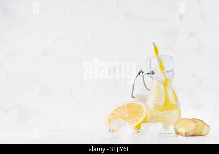 Boisson rafraîchissante aux fruits froids avec citron d'agrumes, bulles lumineuses, glace, gingembre et paille dans une bouteille transparente à yoke en blanc élégant Banque D'Images