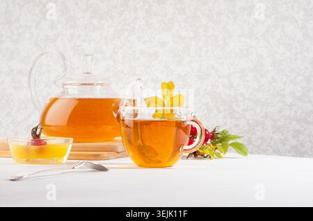 Thé de hanche rose avec théière, tasse, miel, branche de hanche rose d'automne en journée ensoleillée sur table en bois blanc Copy space. Banque D'Images