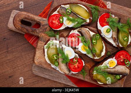 Sandwichs ouverts avec sprats, légumes et herbes, sur une planche de bois, petit déjeuner, collation, Banque D'Images