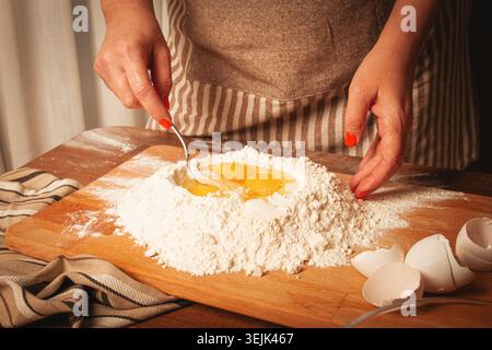 Mélanger les œufs dans la farine pour faire de la pâte pour les pâtes maison dans un cadre de cuisine confortable Banque D'Images