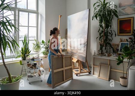 Artiste peintre talentueuse et concentrée travaillant dans le home studio, regardant la peinture sur toile sur chevalet. Banque D'Images