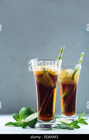 Cocktail rafraîchissant d'été pétillant de cola, glace, citron vert, feuille de menthe sur fond gris contrasté avec espace de copie. Banque D'Images