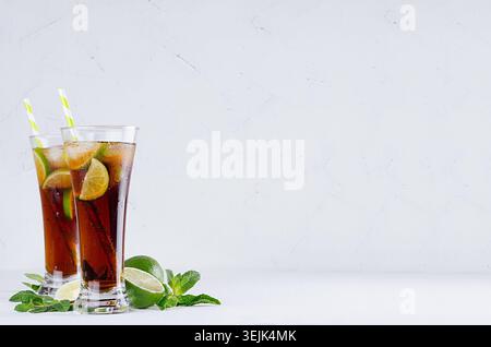 Cocktail rafraîchissant d'été pétillant de cola, glace, citron vert, feuille de menthe sur fond blanc doux avec espace de copie. Banque D'Images