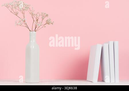 Petites fleurs séchées dans un vase élégant et des livres blancs sur une table en bois et un fond rose pastel doux, espace de copie. Mode maison int Banque D'Images