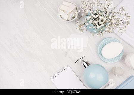 Pose à plat de différents produits cosmétiques et accessoires de couleur argent, bleu pastel et blanc avec de petites fleurs sur bois blanc Banque D'Images