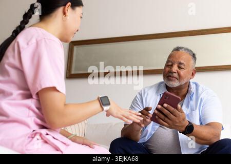 Homme afro-américain senior utilisant le téléphone rouge sur le canapé femme asiatique soignant dans le guide rose-gommage Banque D'Images