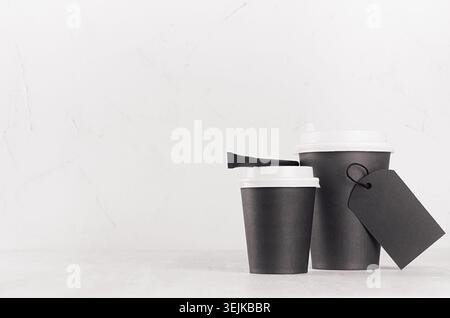 Maquette de café - deux tasses en papier noir avec des chapeaux blancs, étiquette vierge et sac de sucre sur une table en bois blanc avec espace de copie, café Banque D'Images