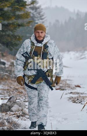 Soldat dans le camouflage d'hiver blanc marchant à travers la forêt enneigée sur patrouille tactique avec fusil Banque D'Images