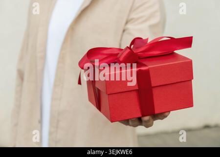 Personne donnant une boîte cadeau rouge avec ruban pour l'anniversaire ou la Saint-Valentin. Banque D'Images