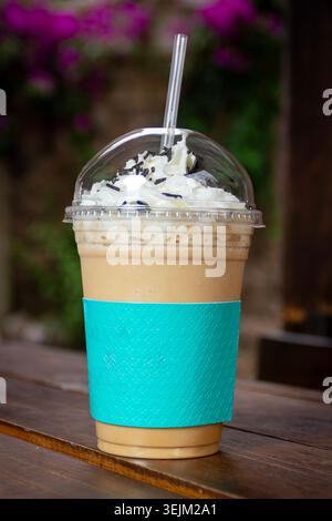 Boisson glacée au café mélangé garnie de crème fouettée servie dans une tasse colorée dans un café en plein air. Banque D'Images