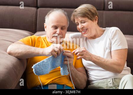 Femme senior enseignant à son mari le tricot. Hommes âgés apprenant le tricot à l'âge de la retraite à la maison. Banque D'Images
