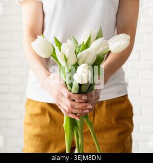 Femme en vêtements jaunes tenant un bouquet de tulipes blanches Banque D'Images