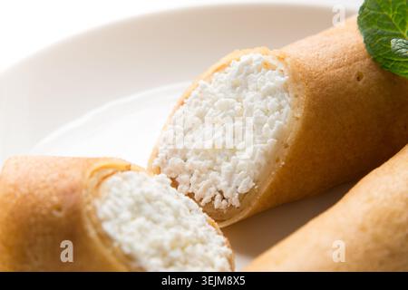 Vue de dessus de crêpes roulées farcies au fromage cottage et garnies de menthe sur une assiette blanche Banque D'Images