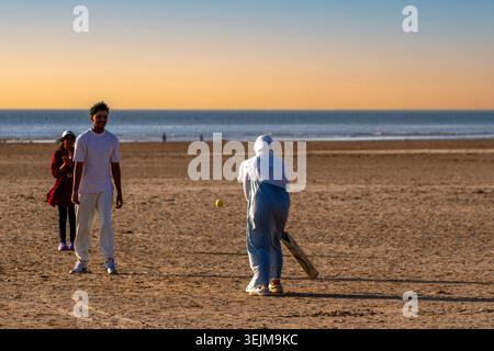 Une famille joue au cricket sur la plage alors que le soleil commence à se coucher. Southport, UK. Banque D'Images