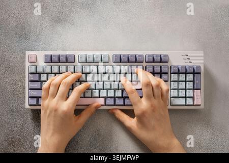 Mains d'adolescent tapant sur le clavier mécanique sur le bureau gris. Banque D'Images