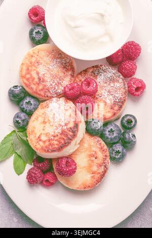 Petit déjeuner, gâteaux au fromage cottage, avec des baies fraîches et de la crème sure, vue de dessus, gros plan, pas de gens, Banque D'Images