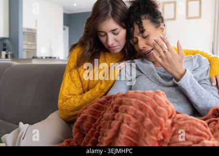 Divers partenaires féminins assis sur le canapé gris dans le salon, réconfortant femme en larmes portant bague. Chaleur, soutien, empathie, ho Banque D'Images