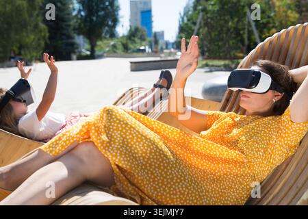 Maman et fille d'enfant jouant au jeu dans des lunettes de réalité virtuelle et détendu dans la ville. copier l'espace. Concept de fami amical Banque D'Images