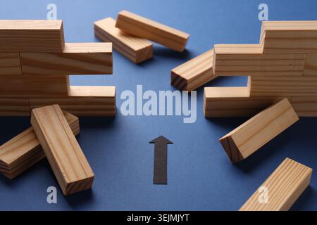 Mur en bois effondré fait de blocs et flèche de papier sur fond bleu, gros plan. Surmonter les obstacles Banque D'Images