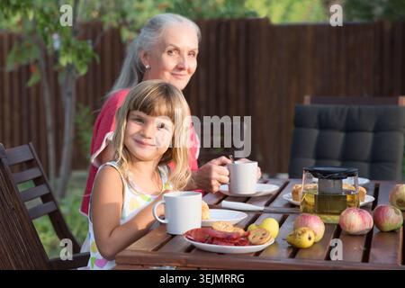 Déjeuner en famille dans le jardin près de la maison un jour d'été. une femme âgée avec une fille adulte et des petits-enfants à la naissance Banque D'Images