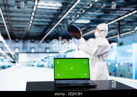 Ordinateur portable à écran isolé utilisé par le concepteur de micropuce dans l'usine de matériel pour étudier les métriques de production de composants. Homme dans l'usine de production de PCB analysant les données de semi-conducteurs avec un ordinateur portable de clé chroma Banque D'Images