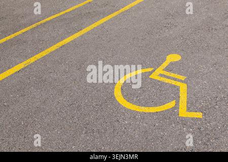 Vue de dessus gros plan d'un symbole jaune pour fauteuil roulant handicapé peint sur une surface de stationnement carrelée de pierre. Symbole international du parking d'accès Banque D'Images