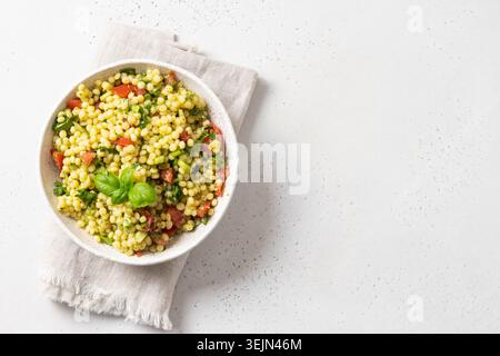 Pâtes ptitim aux légumes, feuilles de basilic décorées sur blanc. Vue de dessus. Espace pour le texte. Banque D'Images