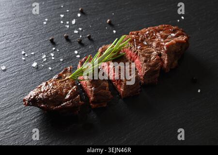 Steak de bœuf marbré grillé frais moyen rare avec romarin sur tableau noir. Banque D'Images