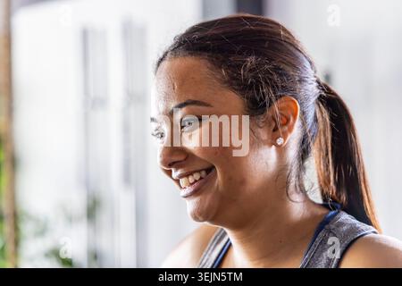 Femme souriant et tournant la tête à gauche dans le gymnase portant haut sans manches avec queue de cheval et boucles d'oreilles clous. Fitness, portrait, studio, AT Banque D'Images