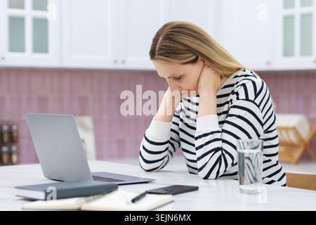 Ménopause. Femme souffrant de douleurs au cou à la table en bois à l'intérieur Banque D'Images
