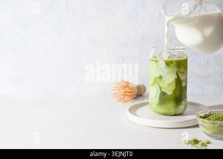 Thé matcha vert glacé et verser du lait dans un verre sur fond blanc.Close up. Orientation horizontale. Banque D'Images