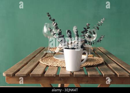 Mug blanc avec des feuilles d'eucalyptus décoratives sèches sur une table en bois Banque D'Images