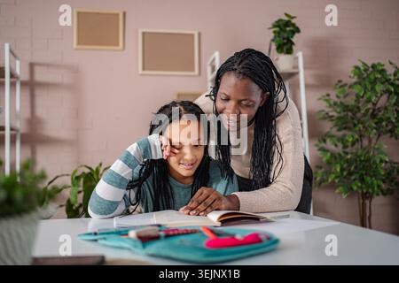 Mère afro-américaine aidant sa fille avec homeschooling Banque D'Images