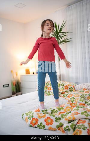 Fille sautant sur le lit jouant à la maison Banque D'Images