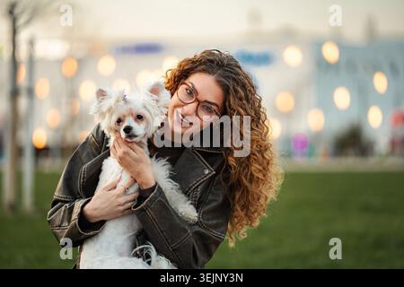 Femme souriant tout en tenant son chien blanc dehors Banque D'Images