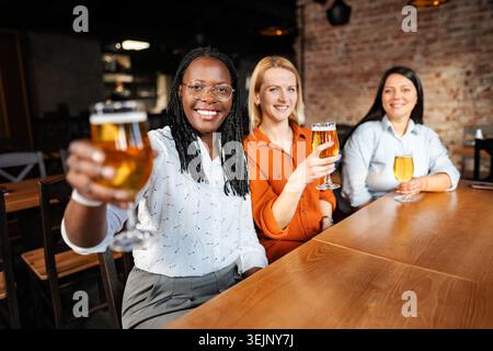Diverses femmes amies appréciant des acclamations avec de la bière au bar Banque D'Images