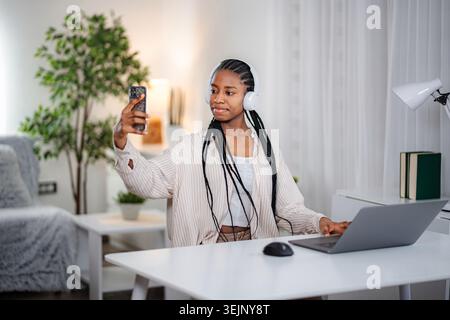 Jeune femme prenant selfie avec smartphone et écouteurs Banque D'Images