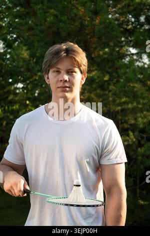 Jeune homme tenant un volant de badminton blanc et une raquette de badminton. Jeu de sports d'été. Extérieur. Banque D'Images