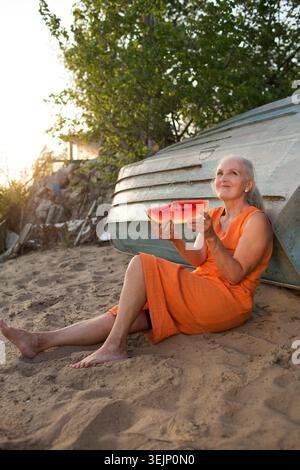 Portrait d'une femme âgée joyeuse avec les cheveux gris avec un morceau de pastèque sur le bord de la mer Banque D'Images
