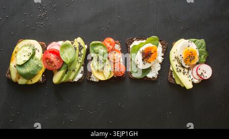 Différents sandwichs avec légumes, œufs, avocat, tomate, pain de seigle sur fond noir de tableau noir. Véh. Supérieure Apéritif pour PA Banque D'Images