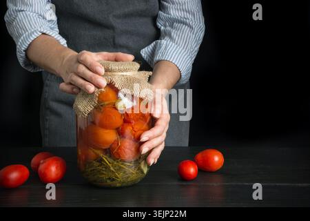 Tomates marinées maison. Femme tenant des légumes en conserve dans des bocaux en verre. Banque D'Images