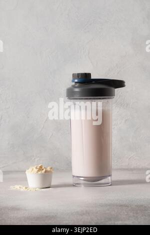 Shake de protéine de lactosérum et haltère sur fond gris. Banque D'Images