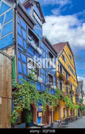 Maisons à colombages bleues et jaunes à Riquewihr Alsace France. Architecture historique traditionnelle sous ciel partiellement nuageux Banque D'Images