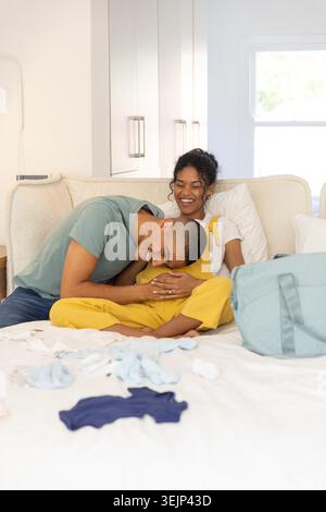 Couple afro-américain assis sur le lit dans la chambre à coucher femme dans une salopette tenant la tête au milieu du sac à couches. Partenaires, ensoleillé, maison, intima Banque D'Images
