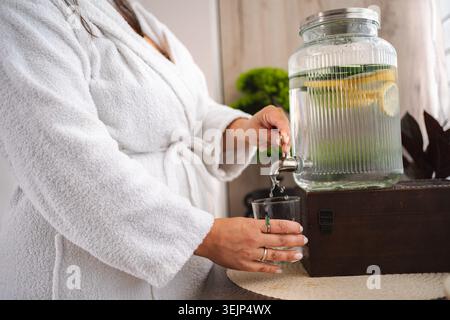 Femme versant de l'eau infusée dans le verre au spa Banque D'Images