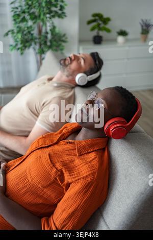 Couple serein se relaxant sur le canapé, profiter de la musique avec des écouteurs Banque D'Images