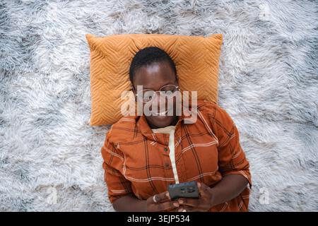 Jeune femme allongée sur un tapis à l'aide d'un smartphone et souriante Banque D'Images