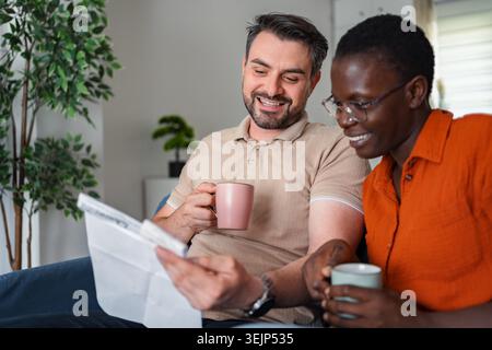 Couple se relaxant sur le canapé, lisant le journal et buvant du café Banque D'Images