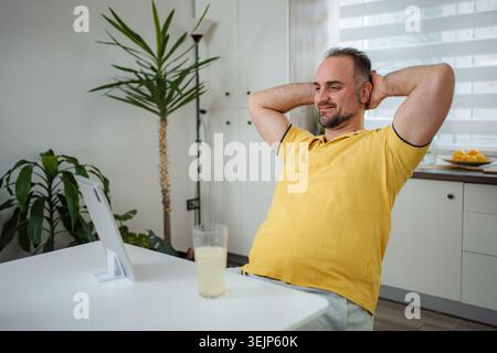 Homme adulte mature se relaxant à la maison regardant la tablette numérique Banque D'Images