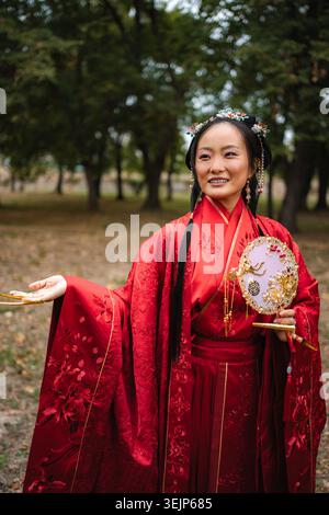 Femme chinoise souriante en robe rouge traditionnelle tenant ventilateur Banque D'Images